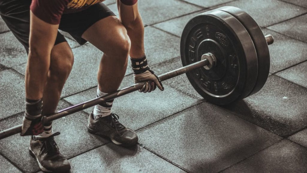 A focused weightlifter prepares to lift a heavy barbell in an indoor gym setting.